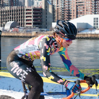 woman races cyclocross in mud, snow, New York City background