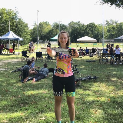 woman holds up sword prize at a bike race